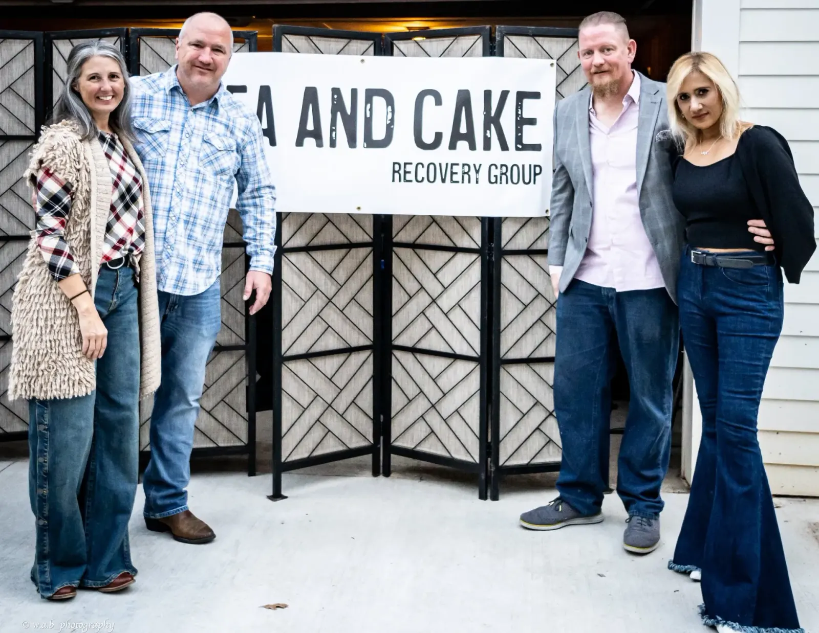 Four Tea and Cake Recovery Group leaders gathered in front of the group's sign